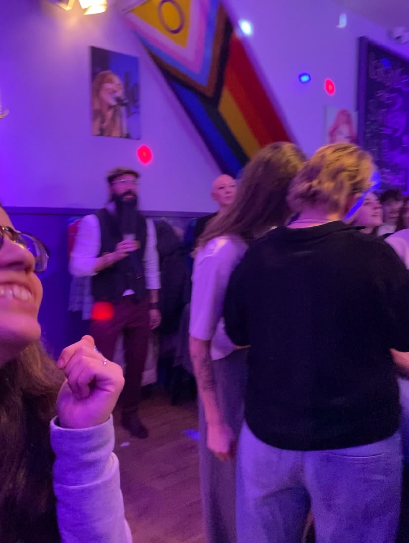 Night out at a queer bar with a Progress Pride flag on the wall