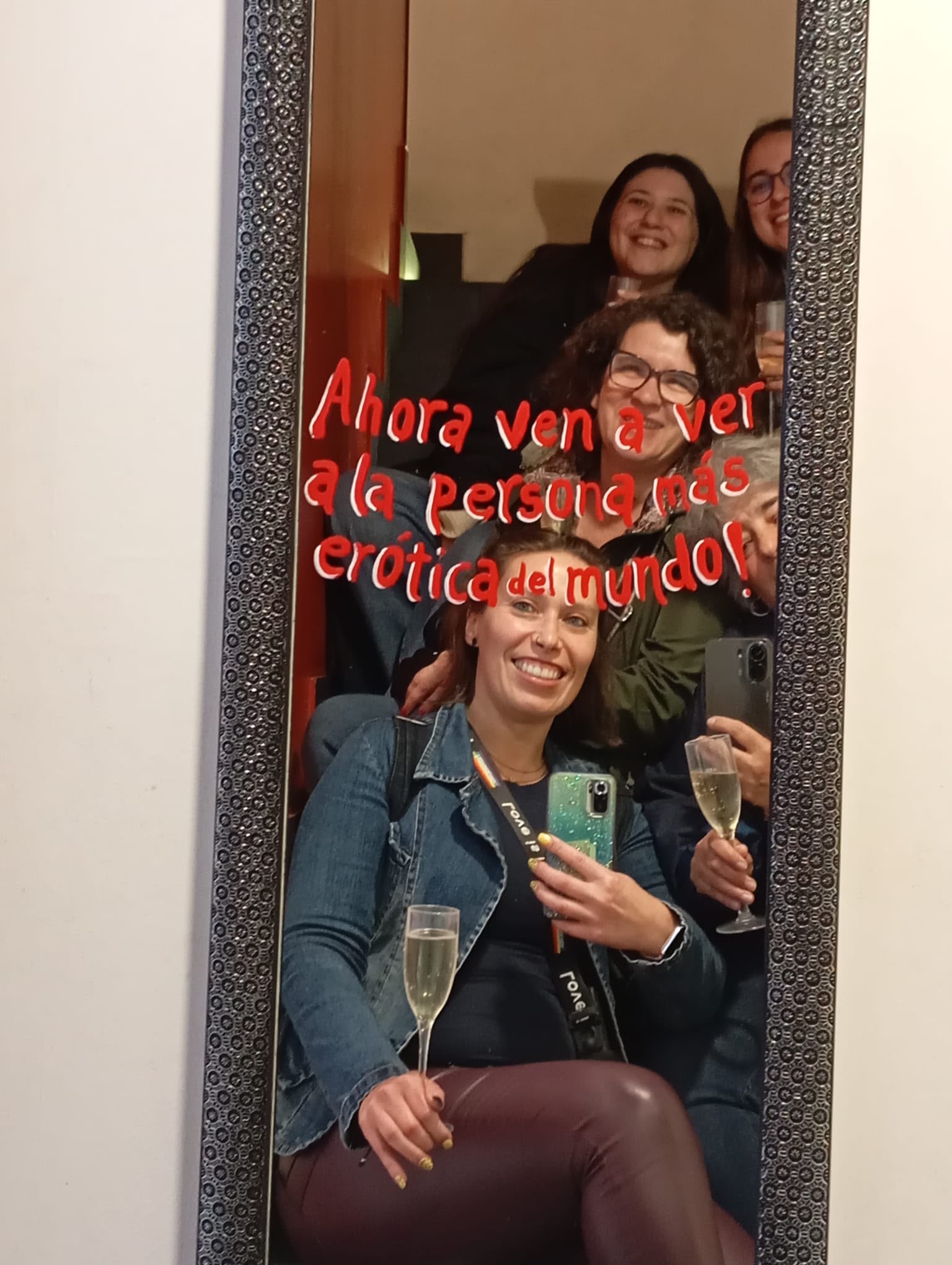 Group selfie in a mirror with champagne, captioned 'Ahora ven a ver a la persona más erótica del mundo'