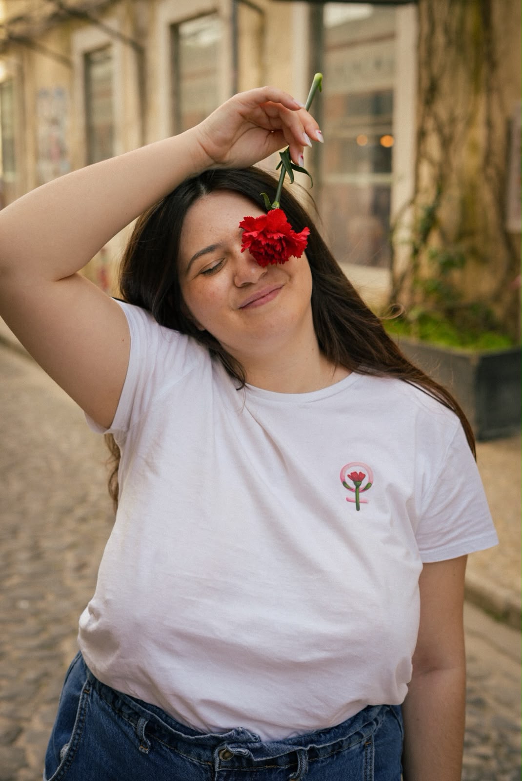 Woman holding a red carnation, wearing a white t-shirt with a feminist symbol and carnation
