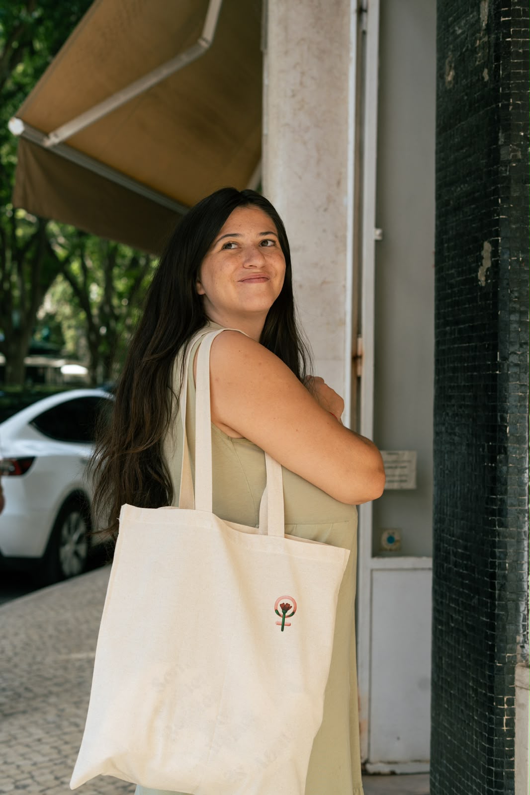 Woman smiling with a canvas tote bag with a feminist symbol and carnation