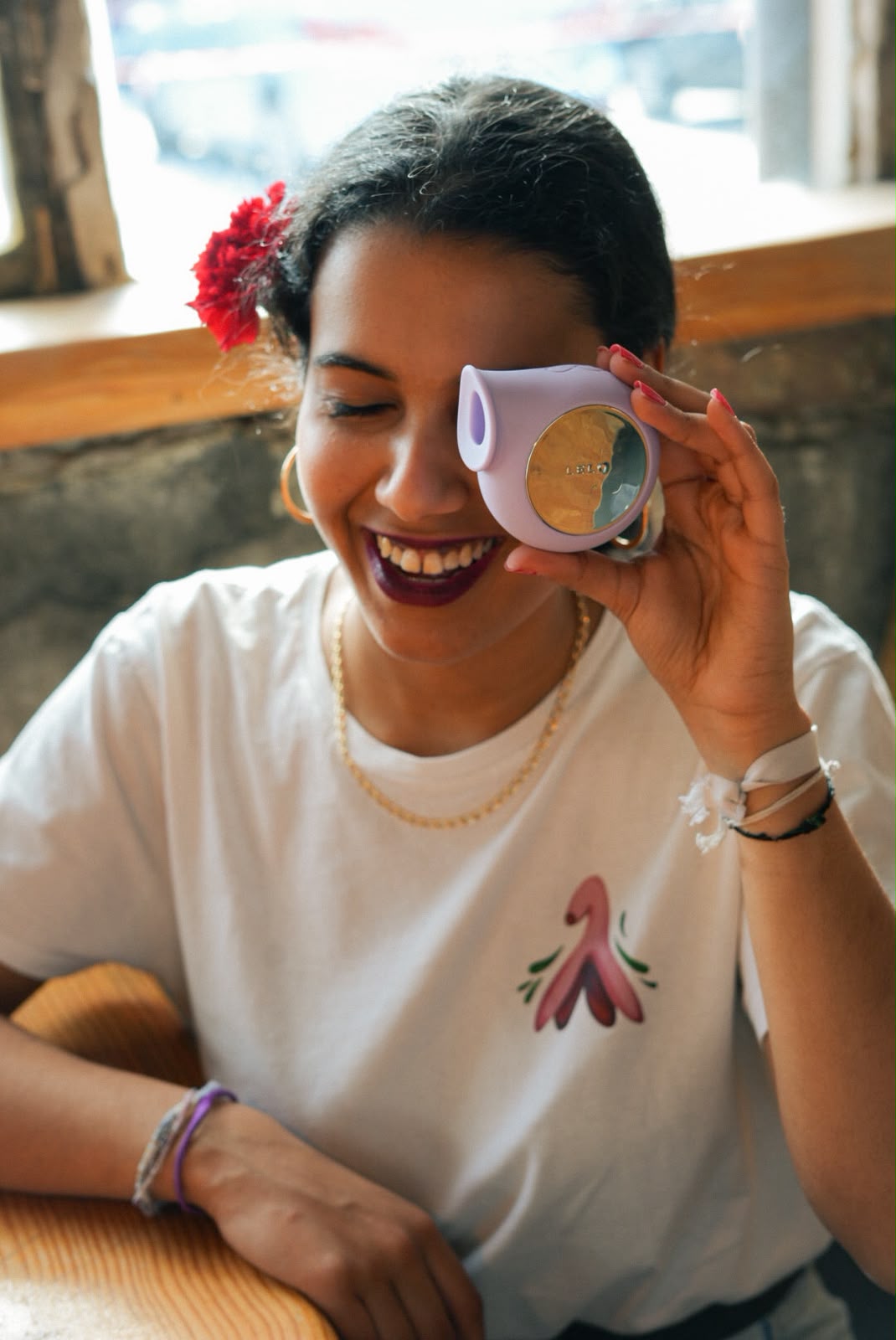 Woman laughing in a white t-shirt with a clitoris illustration, holding a lilac toy over one eye