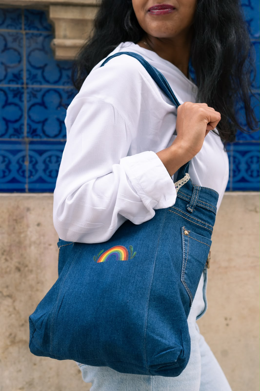 Denim tote bag with a small rainbow print, in front of blue Portuguese tiles