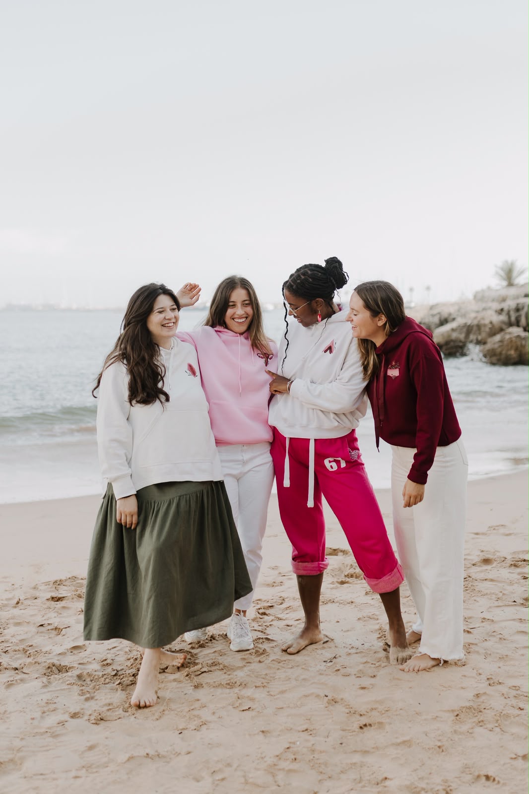 Four friends laughing on the beach wearing hoodies from the collection