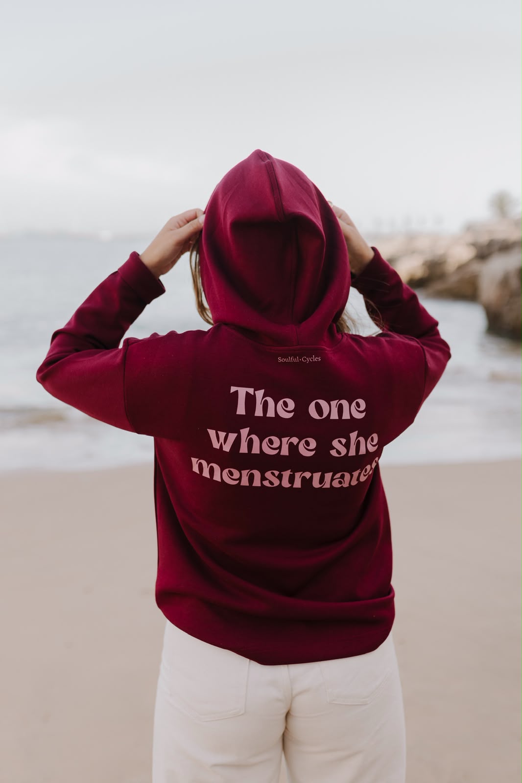 Back of a burgundy hoodie printed 'The one where she menstruates'