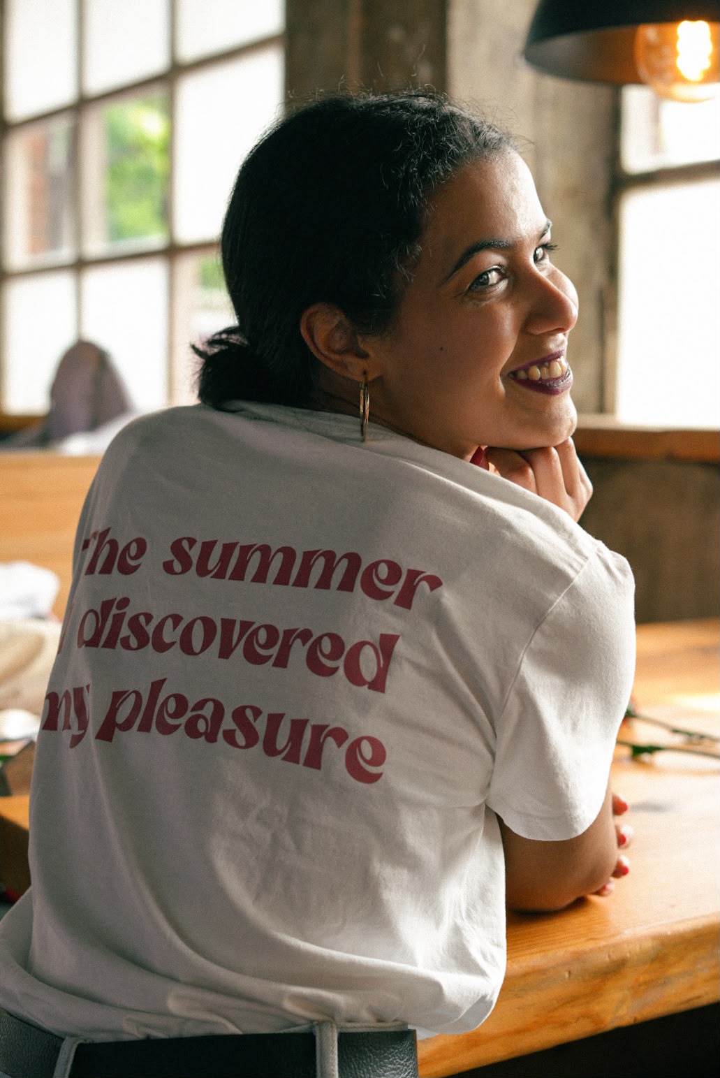 Woman smiling over her shoulder in a t-shirt printed 'The summer I discovered my pleasure'
