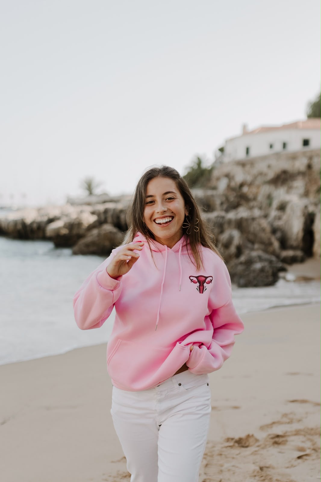 Woman laughing on the beach in a pink hoodie with a uterus illustration