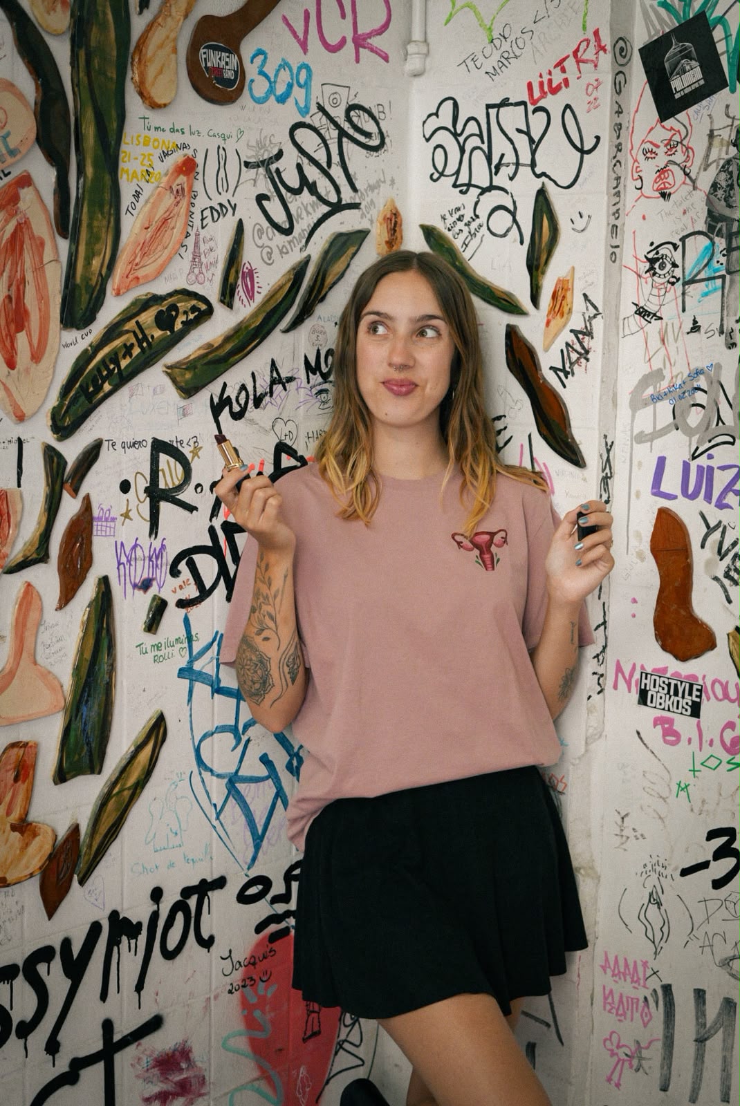 Woman in a pink t-shirt with a uterus illustration, against a graffiti wall