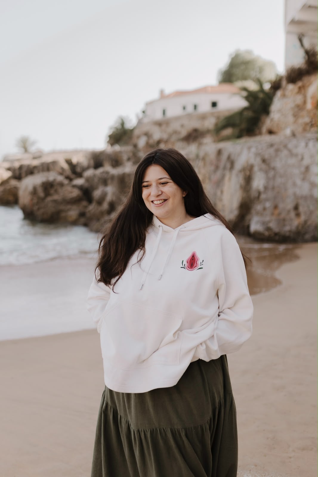 Woman smiling on the beach in a cream hoodie with a vulva illustration