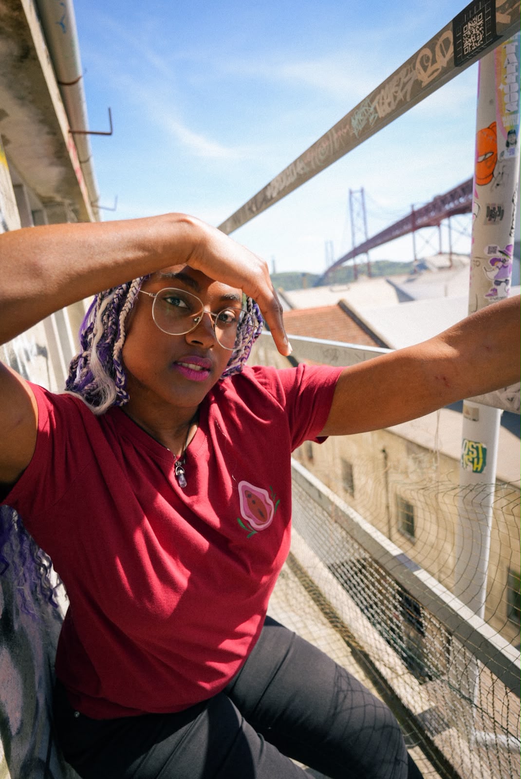 Woman in a red t-shirt with a vulva illustration, with the 25 de Abril bridge behind