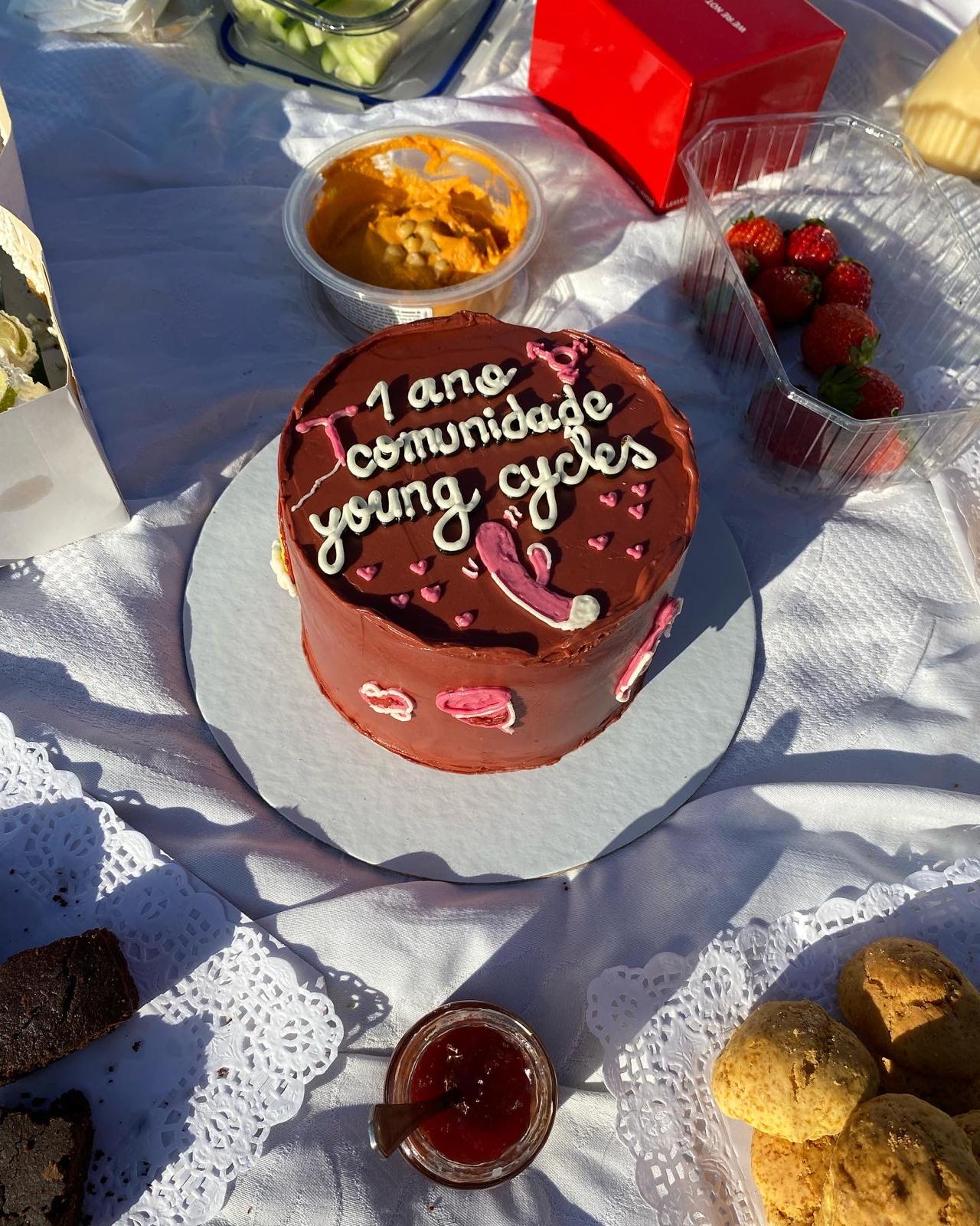 Chocolate cake reading '1 ano comunidade Young Cycles' at a picnic