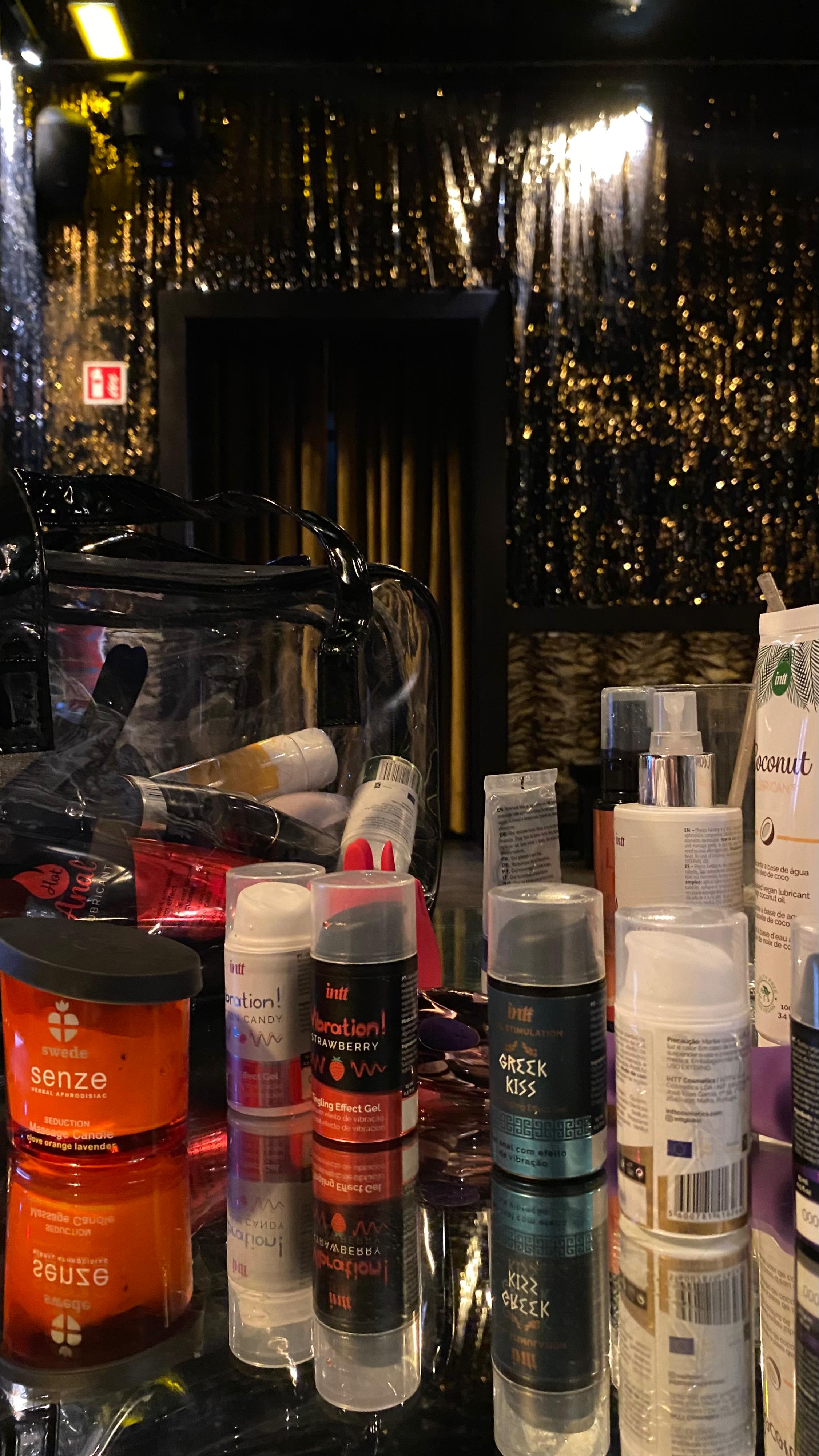 Lubricants, tingling gels and a massage candle lined up on a mirrored table in a glittery room