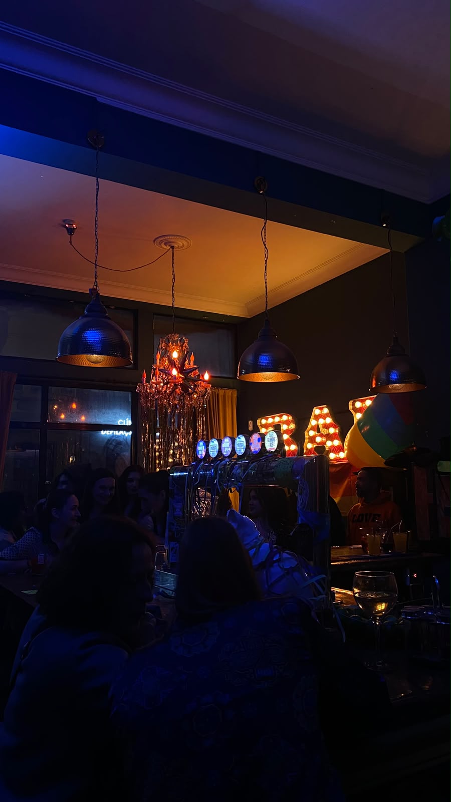Busy bar at night with marquee letters and a rainbow flag