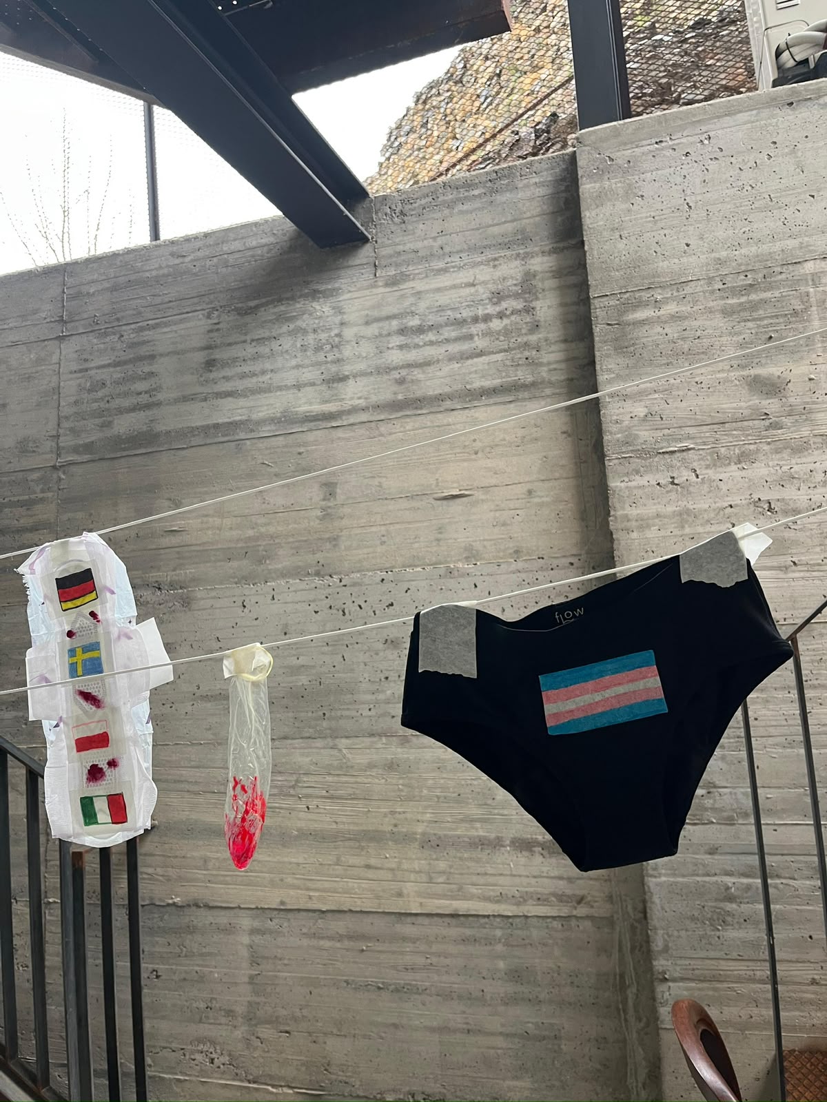 Clothesline with a pad decorated with country flags, a condom and period underwear with a trans flag